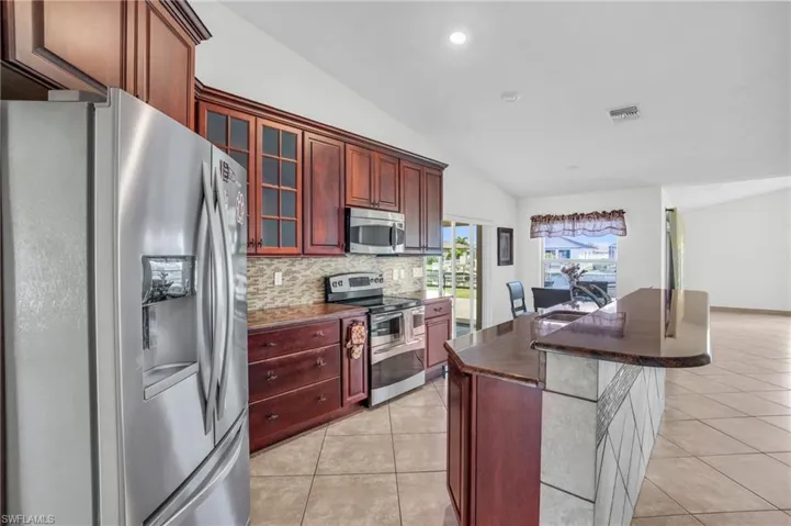 Kitchen with a breakfast bar area, tasteful backsplash, stainless steel appliances, light tile patterned floors, and lofted ceiling