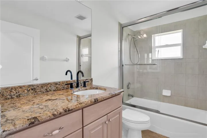 Full bathroom with tile patterned flooring, bath / shower combo with glass door, toilet, and vanity
