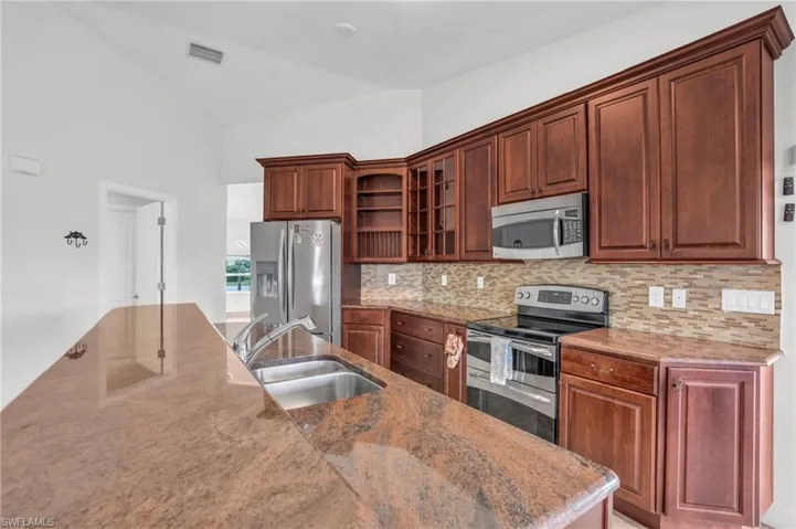 Kitchen with sink, appliances with stainless steel finishes, lofted ceiling, and backsplash