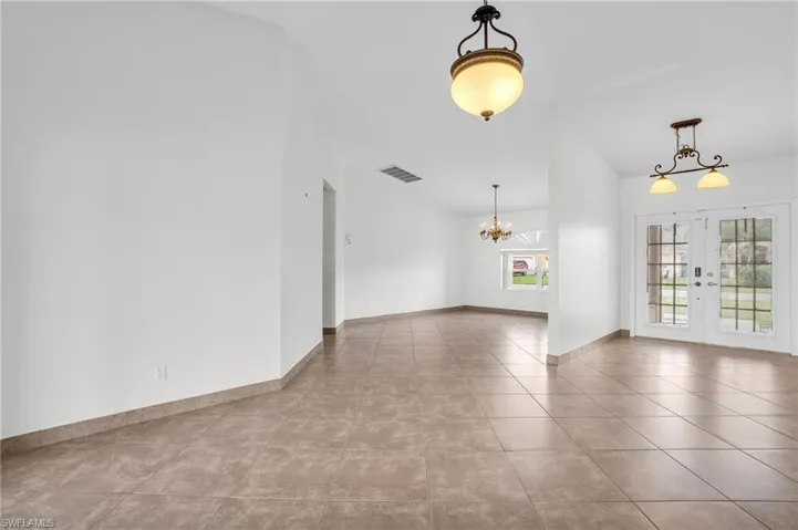 Spare room featuring a notable chandelier, lofted ceiling, light tile patterned floors, and french doors