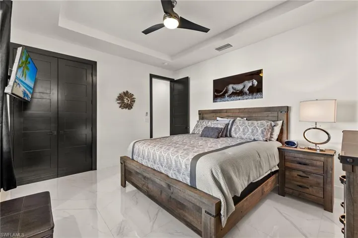 Bedroom with light marble finish flooring, a tray ceiling, and a ceiling fan