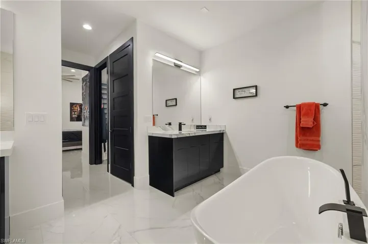 Ensuite bathroom featuring vanity, a soaking tub, light marble finish flooring, and recessed lighting