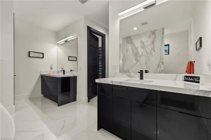 Full bath with light marble finish floors and two vanities