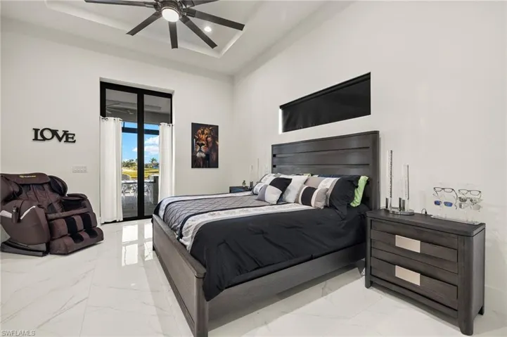 Bedroom with marble tiled flooring, access to exterior, a raised ceiling, ceiling fan, and a towering ceiling
