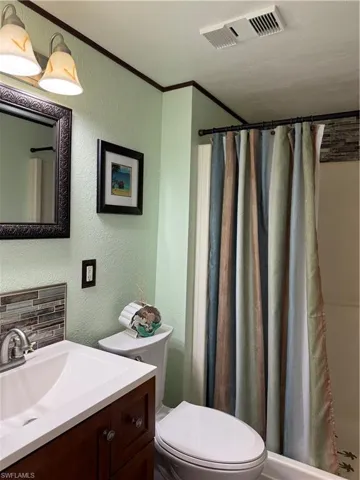 Full bathroom featuring a textured wall, a shower with curtain, vanity, crown molding, and decorative backsplash