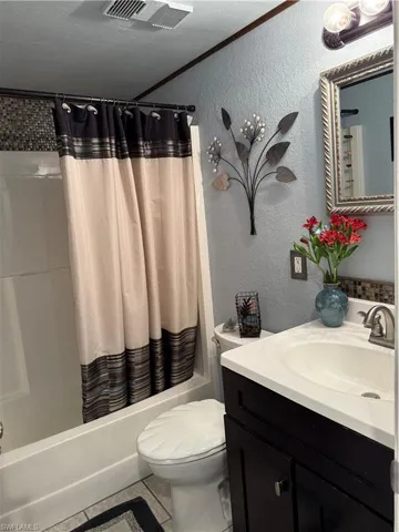 Bathroom with a textured wall, shower / tub combo, vanity, tile patterned flooring, and crown molding