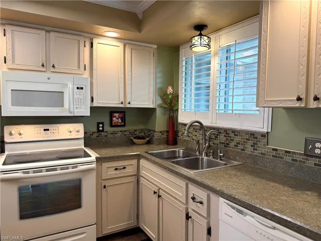 Kitchen with white appliances, dark countertops, ornamental molding, and white cabinetry