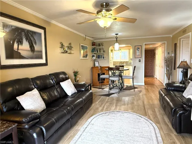Living area featuring light wood-type flooring, ornamental molding, a ceiling fan, and arched walkways