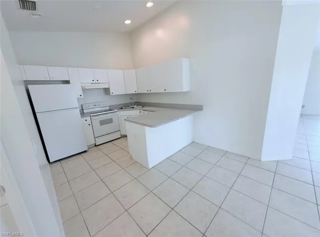 Kitchen with white appliances, a peninsula, white cabinetry, light countertops, and light tile patterned floors