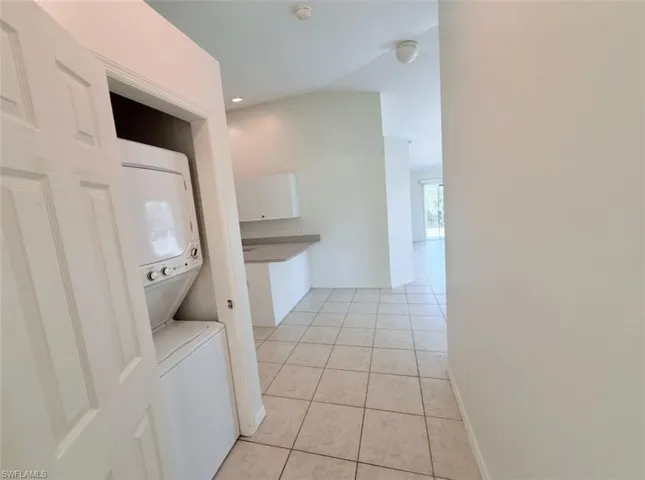 Laundry area featuring stacked washer and clothes dryer, light tile patterned flooring, and recessed lighting