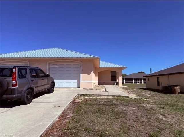 View of property exterior with a metal roof, stucco siding, a garage, and driveway