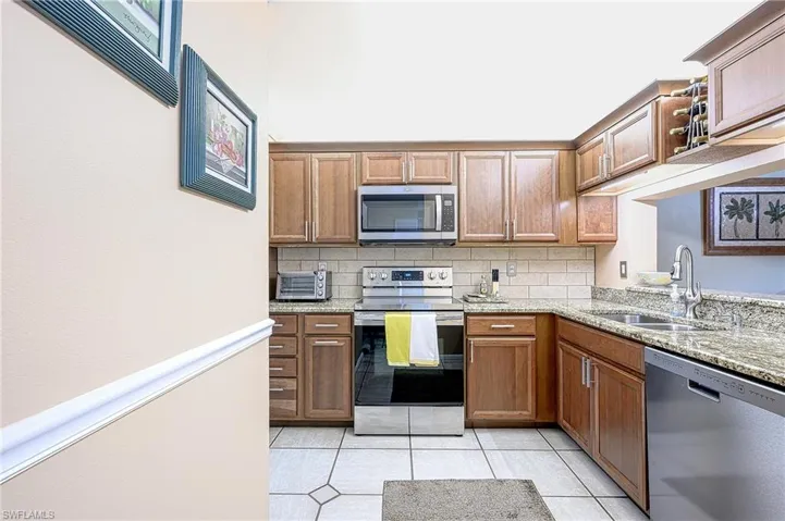 Kitchen featuring sink, light stone counters, backsplash, light tile patterned floors, and appliances with stainless steel finishes
