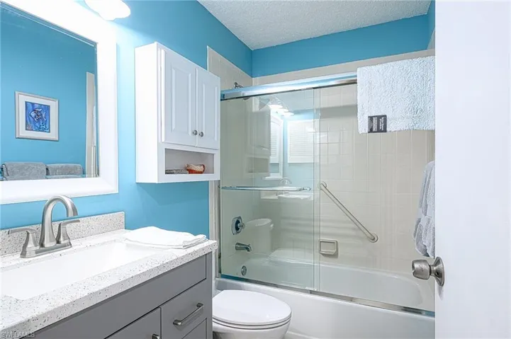 Full bathroom with vanity, bath / shower combo with glass door, a textured ceiling, and toilet