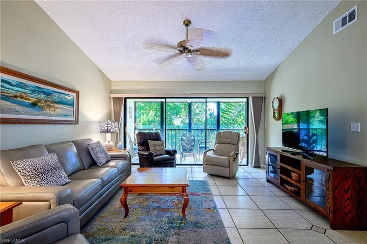 Tiled living room with ceiling fan, lofted ceiling, and a textured ceiling