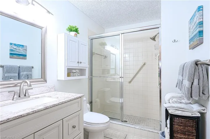 Bathroom with tile patterned flooring, a textured ceiling, toilet, vanity, and a shower with shower door