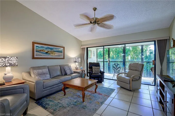Tiled living room featuring vaulted ceiling, ceiling fan, and a textured ceiling
