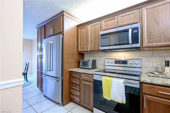 Kitchen featuring tasteful backsplash, light stone counters, light tile patterned floors, and stainless steel appliances