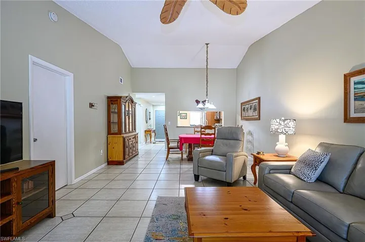 Tiled living room featuring ceiling fan with notable chandelier and vaulted ceiling