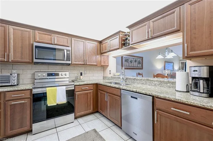 Kitchen featuring sink, light stone countertops, light tile patterned floors, appliances with stainless steel finishes, and tasteful backsplash