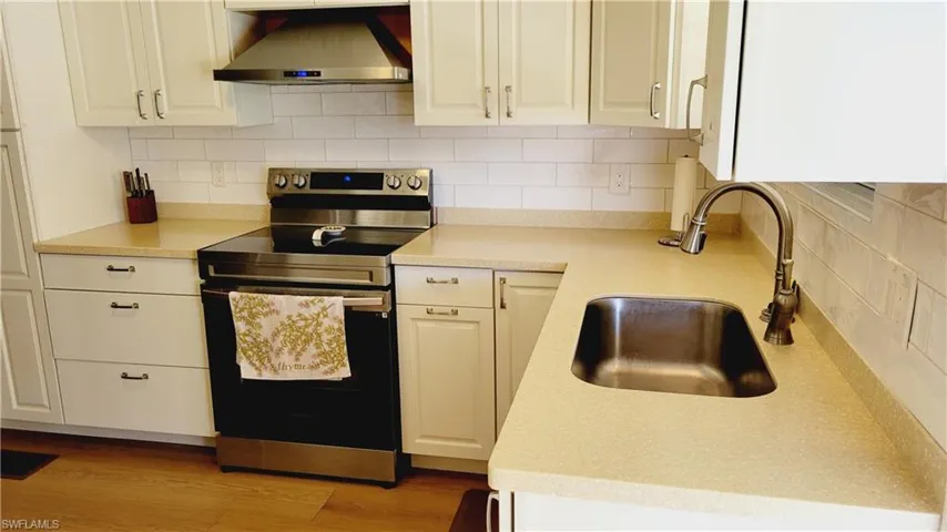 Kitchen featuring stainless steel electric range oven, wall chimney range hood, a sink, tasteful backsplash, and light countertops