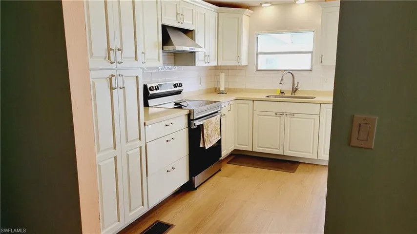 Kitchen featuring exhaust hood, stainless steel electric stove, a sink, light wood finished floors, and tasteful tile backsplash