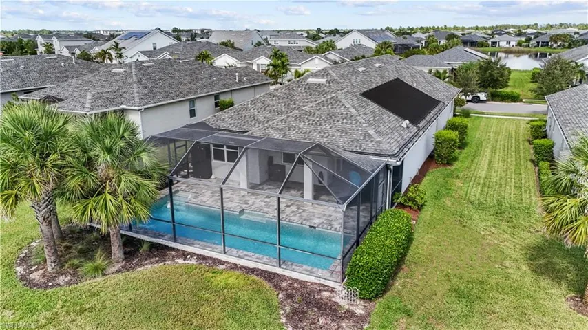 Screen-enclosed swimming pool with paver decking, adjacent patio space, and solar pool heating panels on the roof. 16160 Bluestem Ln. Babcock Ranch, FL 33982