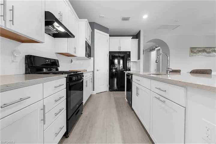 White shaker cabinetry, light-toned countertops, black appliance suite, white subway tile backsplash, and wood-finish flooring. 16160 Bluestem Ln. Babcock Ranch, FL 33982