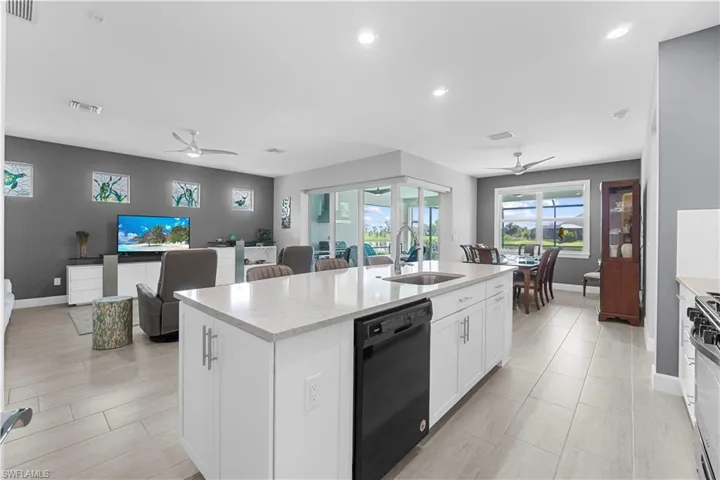 White kitchen island with a built-in single bowl sink and stainless steel faucet, light-toned tile flooring, recessed lighting, and a dining area with a window. 16160 Bluestem Ln. Babcock Ranch, FL 33982
