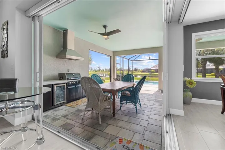 Expansive screened lanai with a ceiling fan, outdoor kitchen featuring a range hood and built-in grill, and paved flooring. 16160 Bluestem Ln. Babcock Ranch, FL 33982