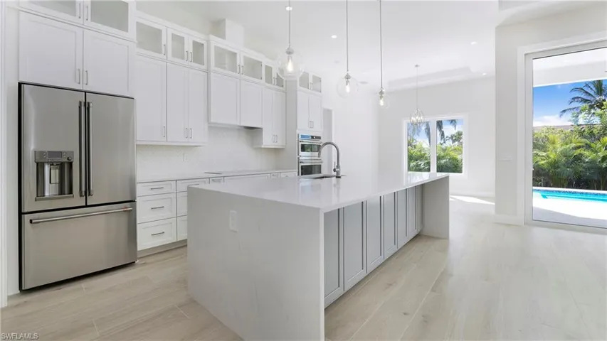 Kitchen with stainless steel appliances, tasteful backsplash, light stone countertops, light wood-style floors, and glass insert cabinets