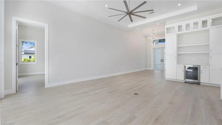 Unfurnished living room featuring light wood-style floors, wine cooler, recessed lighting, a chandelier, and a tray ceiling