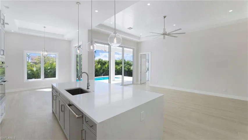 Kitchen with a tray ceiling, pendant lighting, an island with sink, light wood-type flooring, and open floor plan