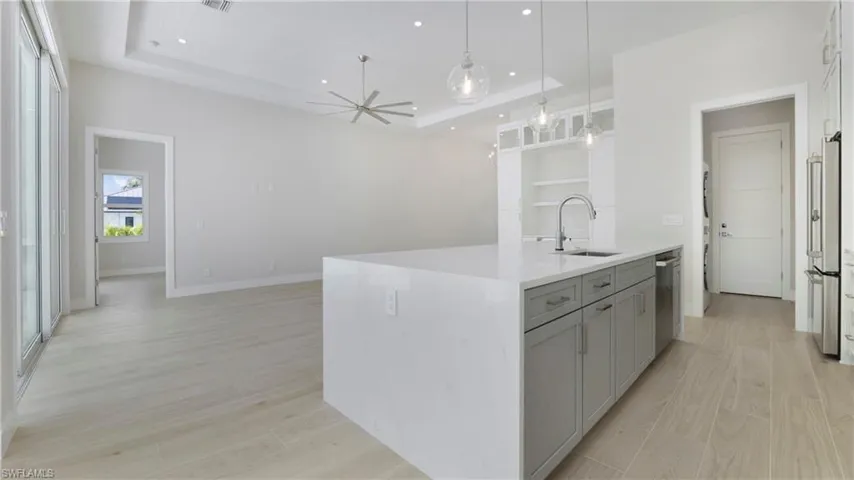Kitchen with a raised ceiling, gray cabinetry, decorative light fixtures, light wood-style flooring, and a ceiling fan
