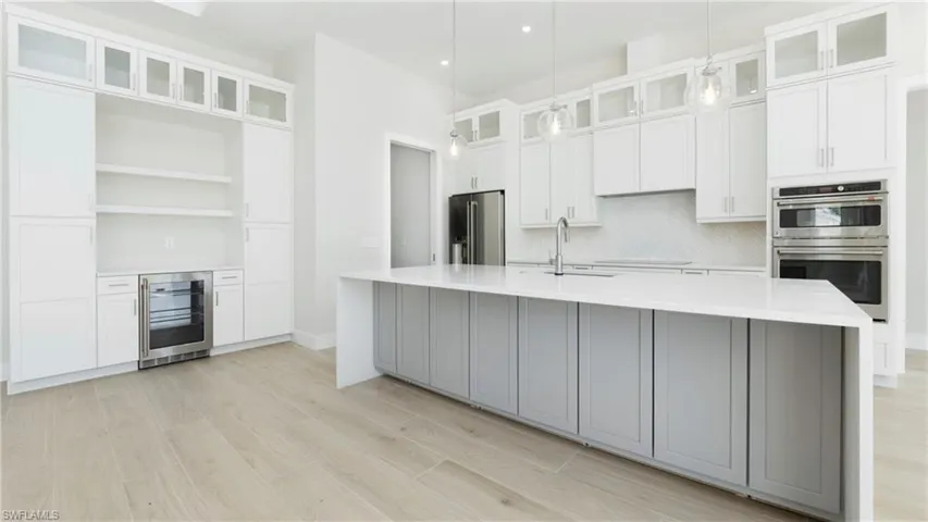 Kitchen with glass insert cabinets, beverage cooler, stainless steel appliances, decorative backsplash, and pendant lighting