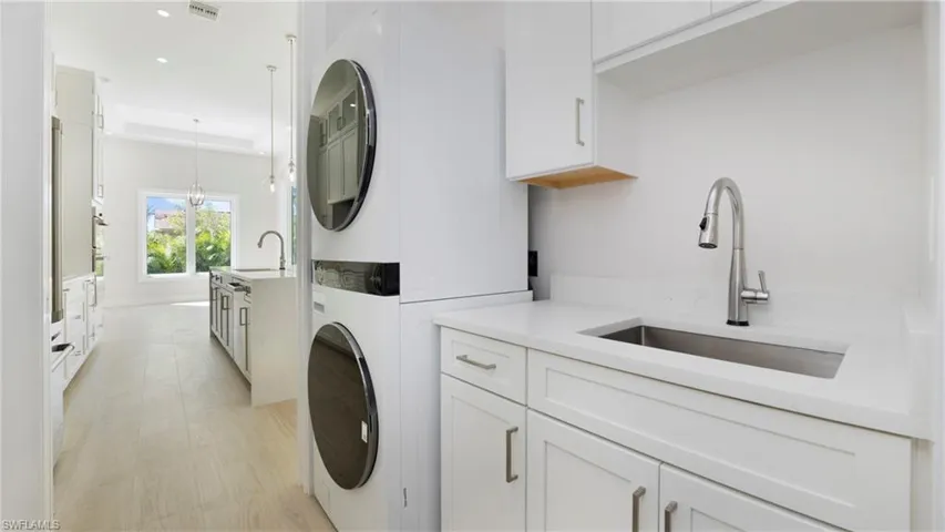 Washroom featuring stacked washer / drying machine, light wood-type flooring, cabinet space, recessed lighting, and a chandelier