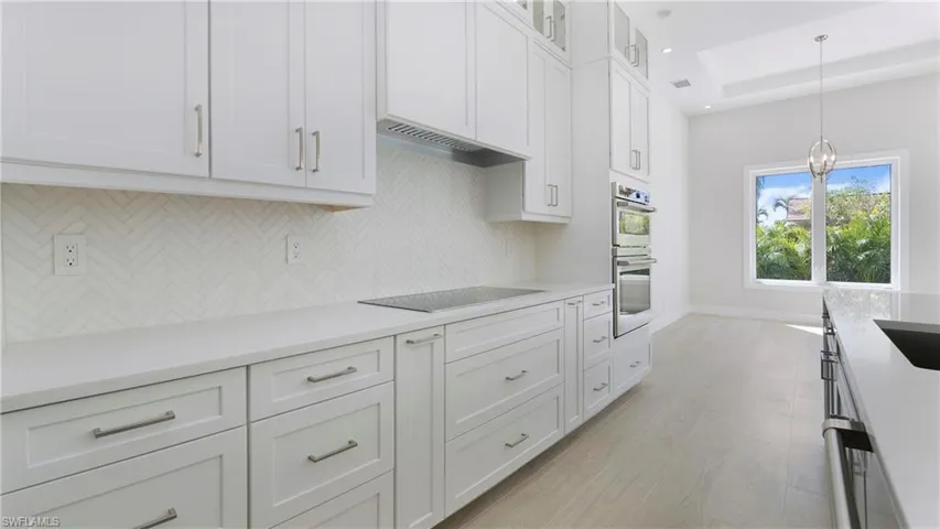 Kitchen with decorative backsplash, white cabinets, decorative light fixtures, and light wood finished floors