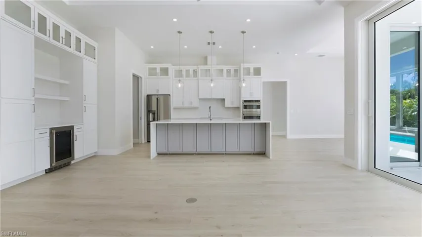 Kitchen with pendant lighting, a center island with sink, glass insert cabinets, light wood-style floors, and white cabinetry