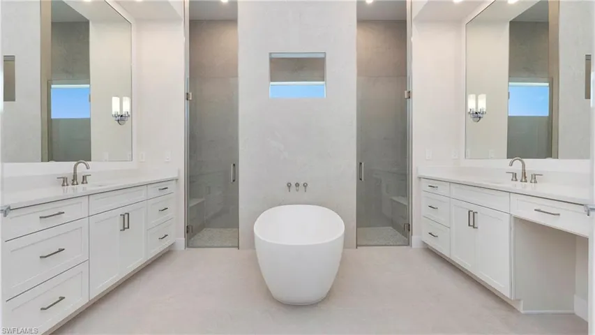 Full bathroom with a stall shower, a freestanding tub, two vanities, and light tile patterned floors