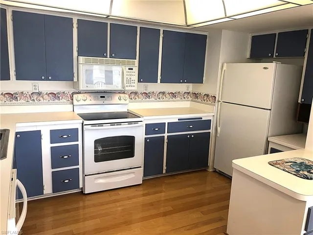Kitchen featuring white appliances, light wood finished floors, blue cabinetry, and light countertops