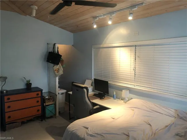 Carpeted bedroom featuring rail lighting, wooden ceiling, and an office area