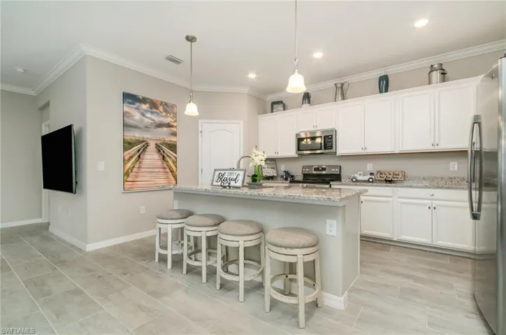 Kitchen with white cabinetry, light stone countertops, ornamental molding, and appliances with stainless steel finishes