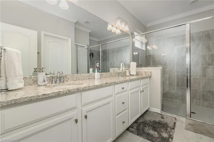 Bathroom featuring crown molding, a sink, a stall shower, visible vents, and double vanity