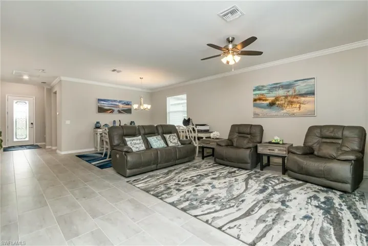Living area with crown molding, baseboards, light tile patterned floors, ceiling fan with notable chandelier, and visible vents