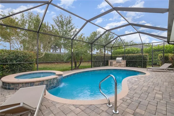 View of pool with glass enclosure, a pool with connected hot tub, exterior kitchen, and a patio