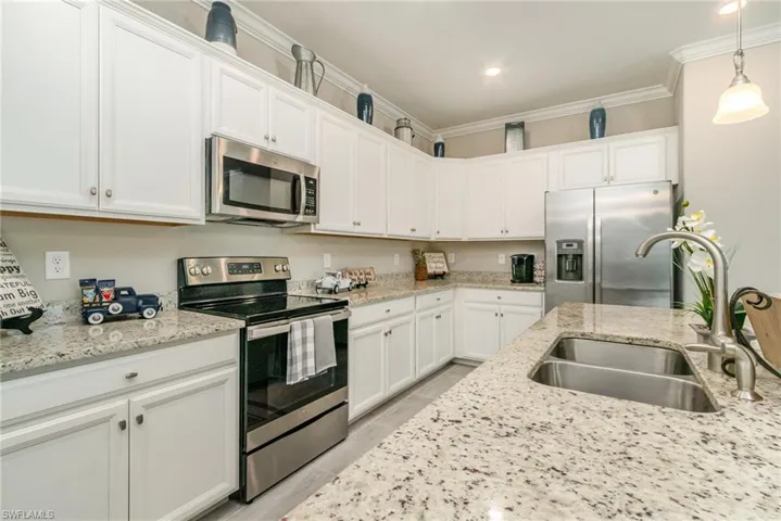 Kitchen with ornamental molding, stainless steel appliances, hanging light fixtures, a sink, and white cabinets
