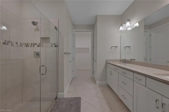 Full bath featuring double vanity, a stall shower, a walk in closet, and light tile patterned floors