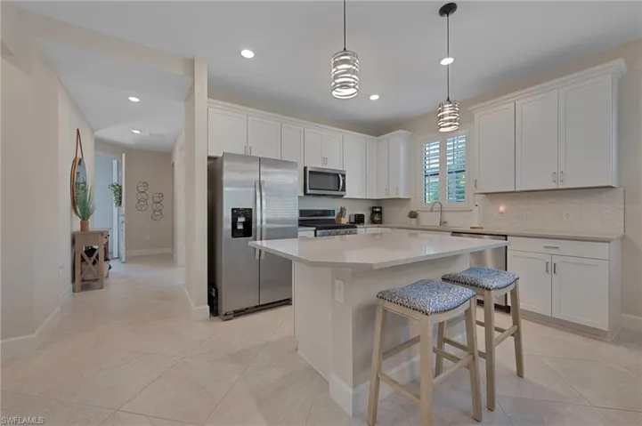 Kitchen featuring appliances with stainless steel finishes, a breakfast bar area, hanging light fixtures, a center island, and white cabinetry
