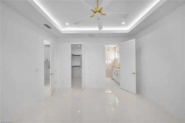 Unfurnished bedroom with a spacious closet, a tray ceiling, a ceiling fan, recessed lighting, and connected bathroom