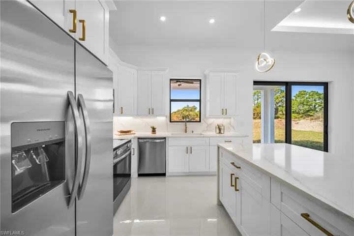 Kitchen featuring stainless steel appliances, white cabinets, light stone countertops, and hanging light fixtures