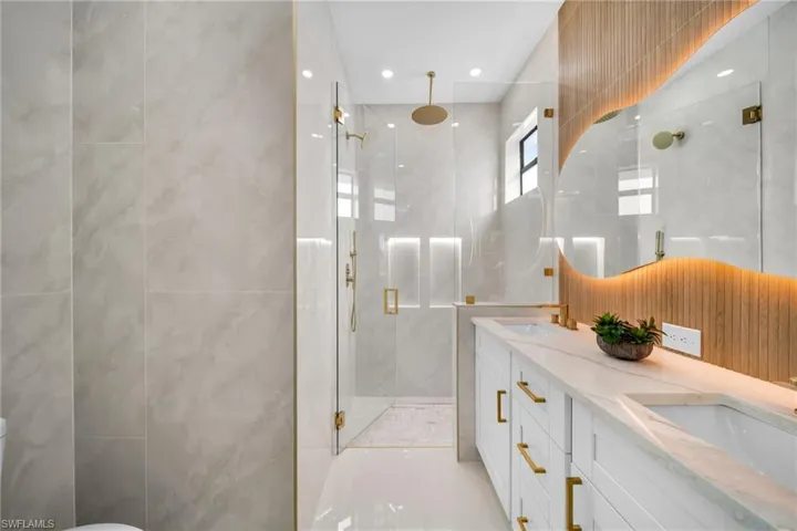 Bathroom with double vanity, a marble finish shower, tile walls, and recessed lighting